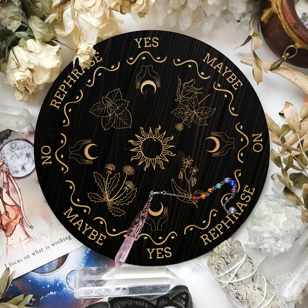 Black Pendulum Board with engraved images of the sun, crescent moons cupped in hands and divination phrases such a yes, no & rephrased laid out with the divination pendant laid on-top.