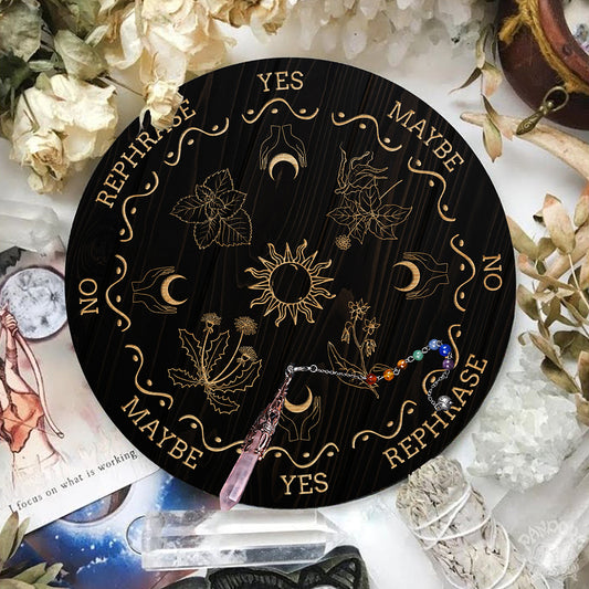 Black Pendulum Board with engraved images of the sun, crescent moons cupped in hands and divination phrases such a yes, no & rephrased laid out with the divination pendant laid on-top.